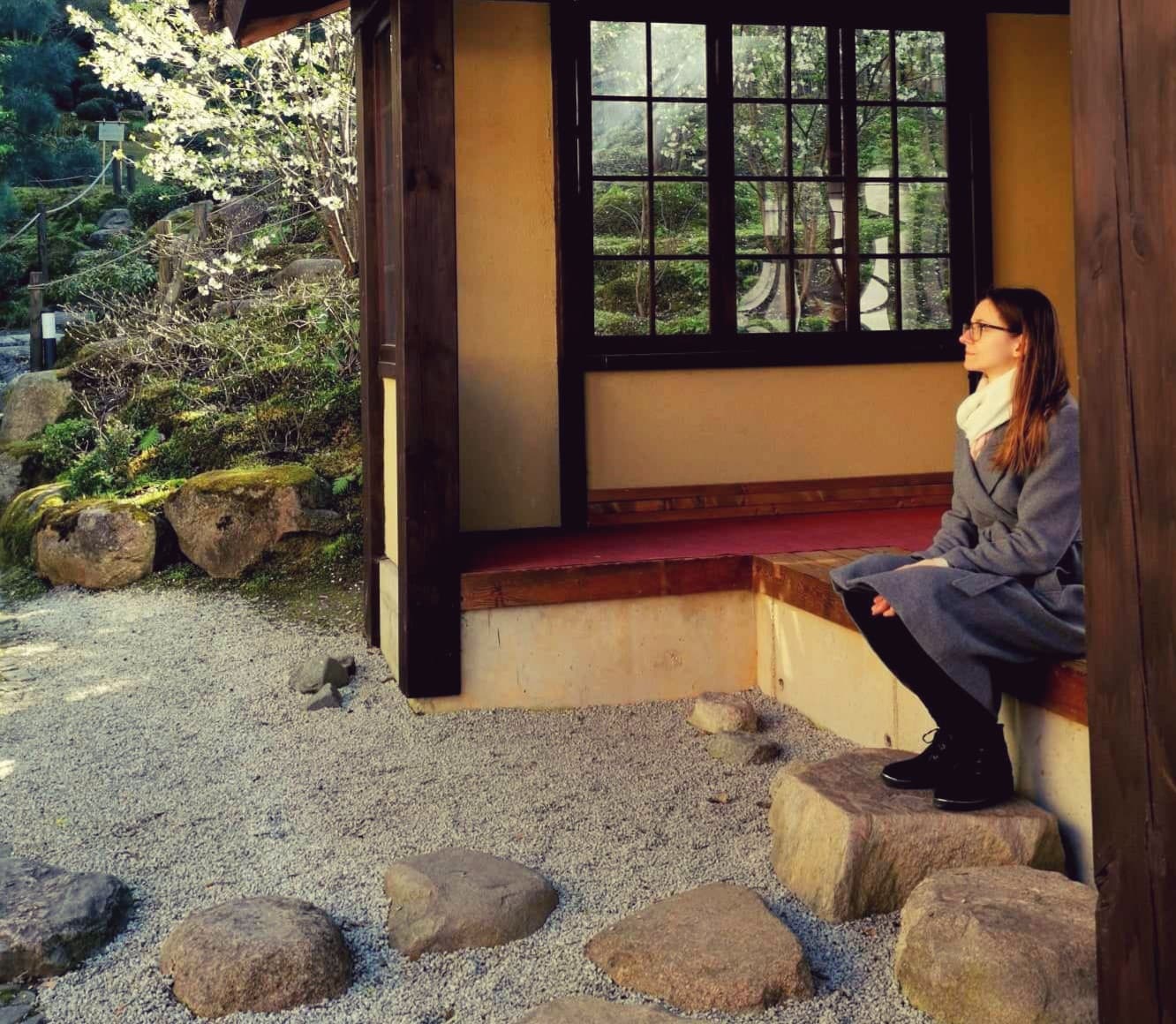 Ausrine sitting at the edge of a wooden pavilion in a Japanese garden